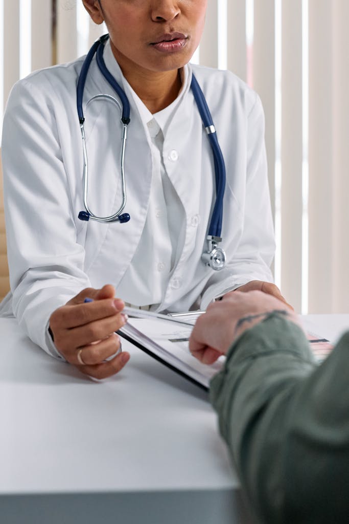A doctor in a white coat consulting a patient at a table with medical documents.