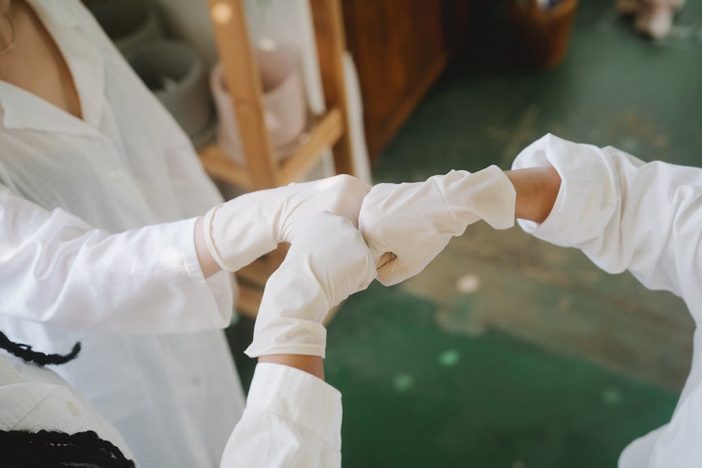 Close-up of healthcare professionals in white lab coats and gloves fist bumping in a laboratory environment.